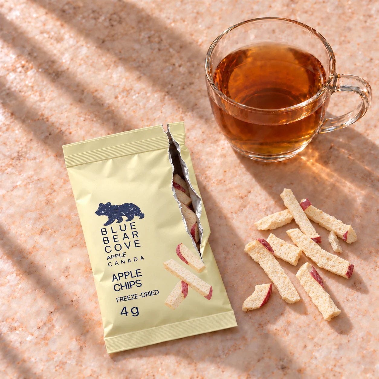 A yellow apple chip sachet beside a cup of tea and thin apple strips.
