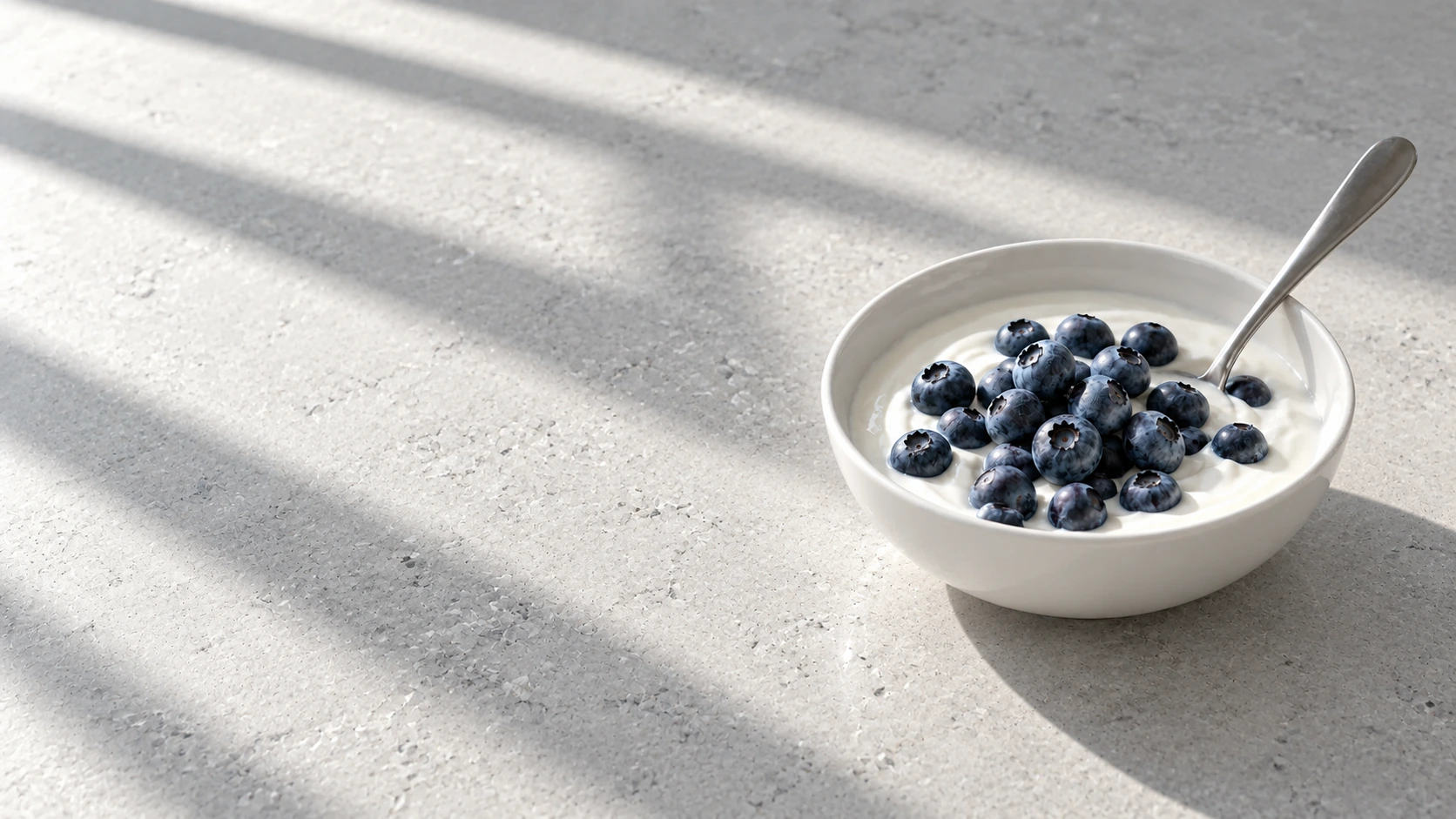 Yogurt and blueberries in a simple white bowl on a bright stone surface