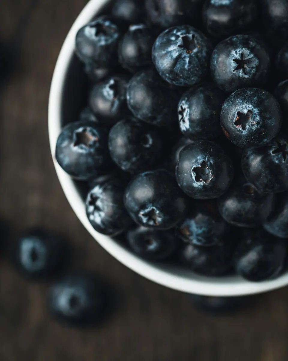 A white bowl of blueberries on a dark table photographed in Winnipeg, Canada