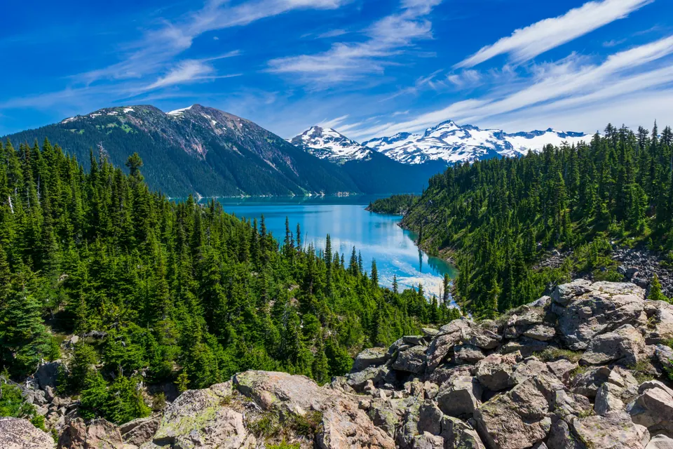 Turquoise Garibaldi Lake surrounded by evergreen forest and snowy mountains in British Columbia